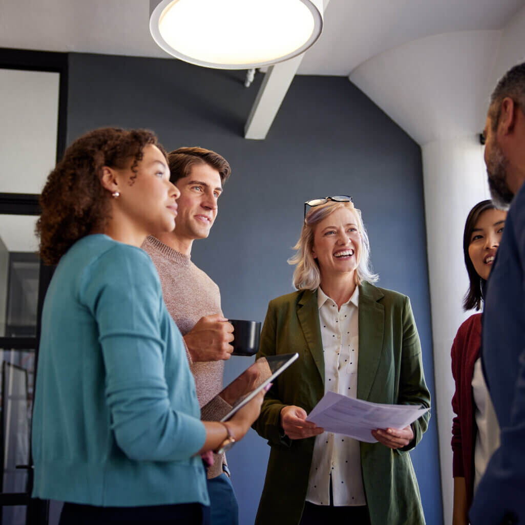 Group of colleagues engaging in a friendly conversation at work. Professional business team smiling and sharing ideas in a casual office setting. Business people having a relaxed discussion in a modern workplace while smiling and talking to each others.
